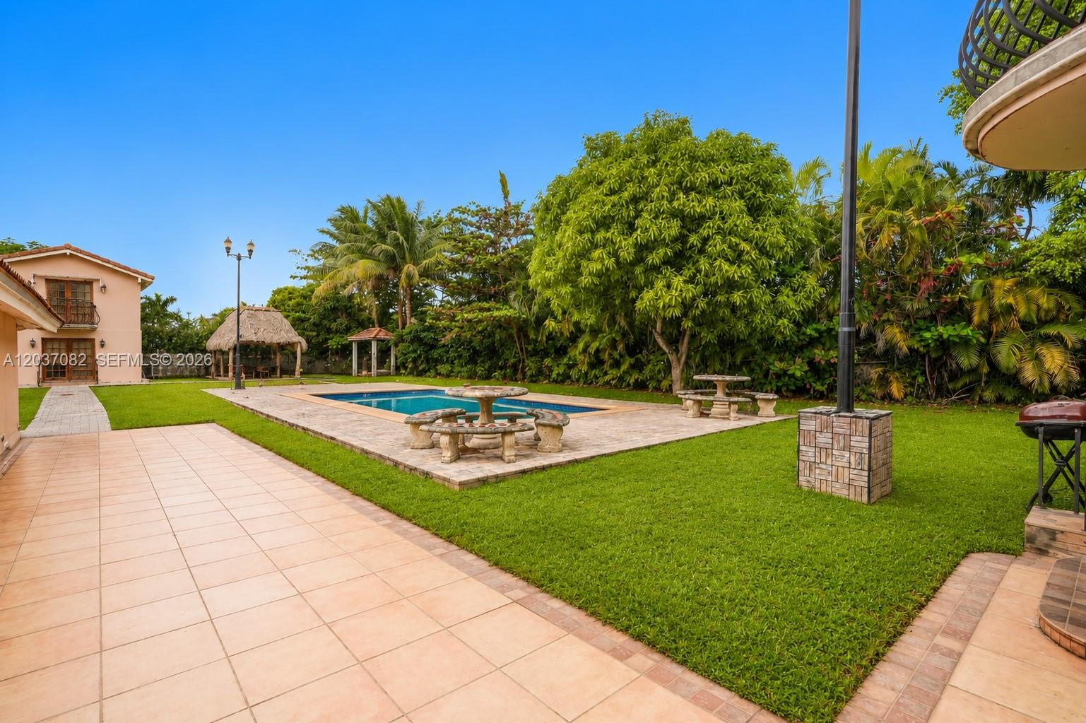 A backyard features a swimming pool, stone patio, lawn, and a thatched-roof gazebo — 300 SW 123rd Ave, Miami FL 33184, MIAMI, FL