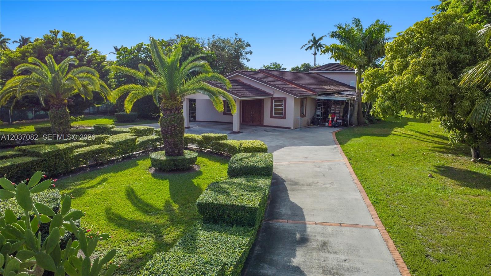 An exterior view of a single-story house with a concrete driveway and manicured hedges — 300 SW 123rd Ave, Miami FL 33184, MIAMI, FL