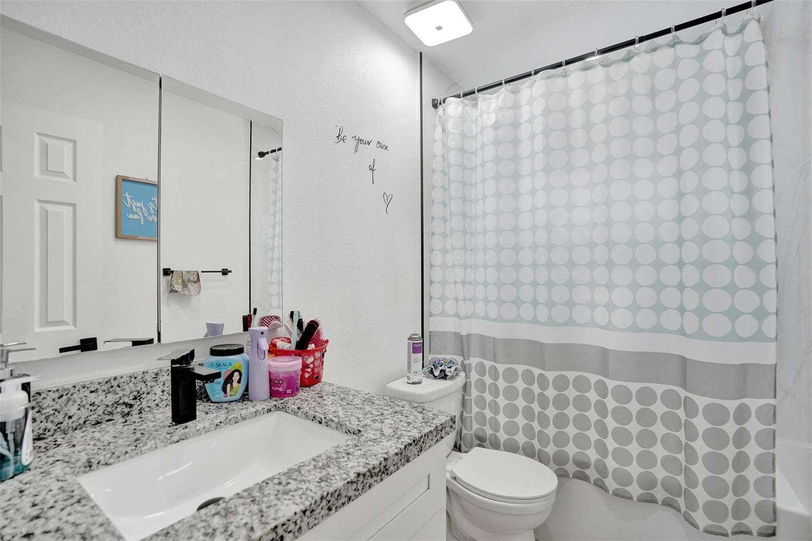 A bathroom features a granite vanity, a white sink, a toilet, and a polka-dot shower curtain — 209 NE 9th Street, Pompano Beach FL 33060, POMPANO BEACH, FL