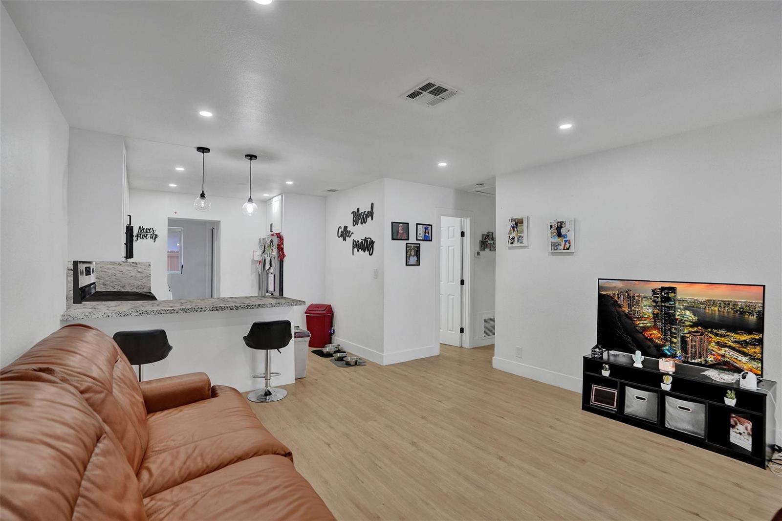 A living room with light wood flooring, a leather sofa, and an open kitchen area — 209 NE 9th Street, Pompano Beach FL 33060, POMPANO BEACH, FL