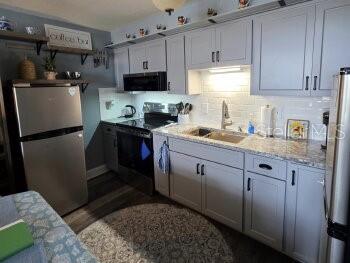 A kitchen features gray cabinets, stainless steel appliances, granite countertops, and a subway tile backsplash — 4363 TAHITIAN GARDENS CIRCLE UNIT G, HOLIDAY, FL