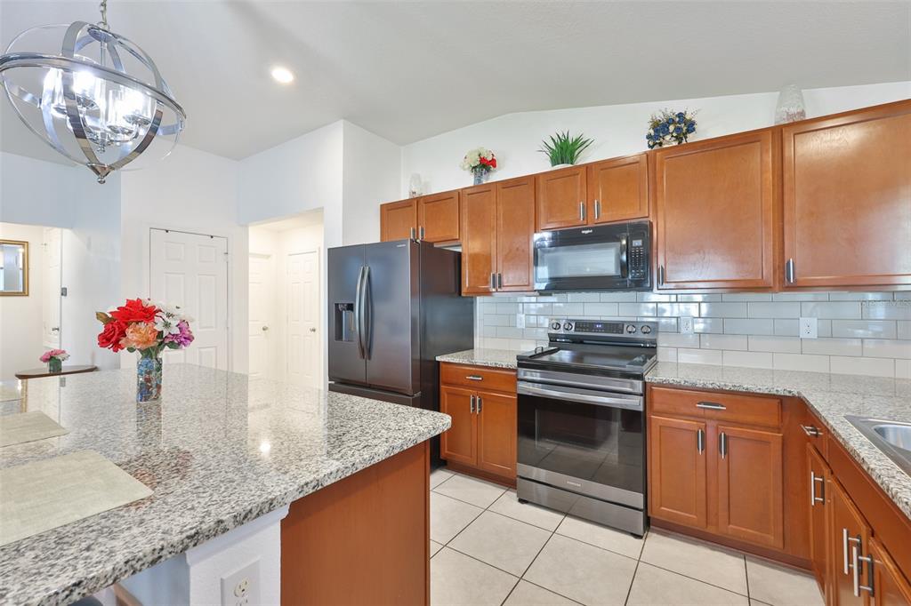 A kitchen features wood cabinets, granite countertops, stainless steel appliances, and a large center island — 7640 MUSCOVY DRIVE, LAKELAND, FL