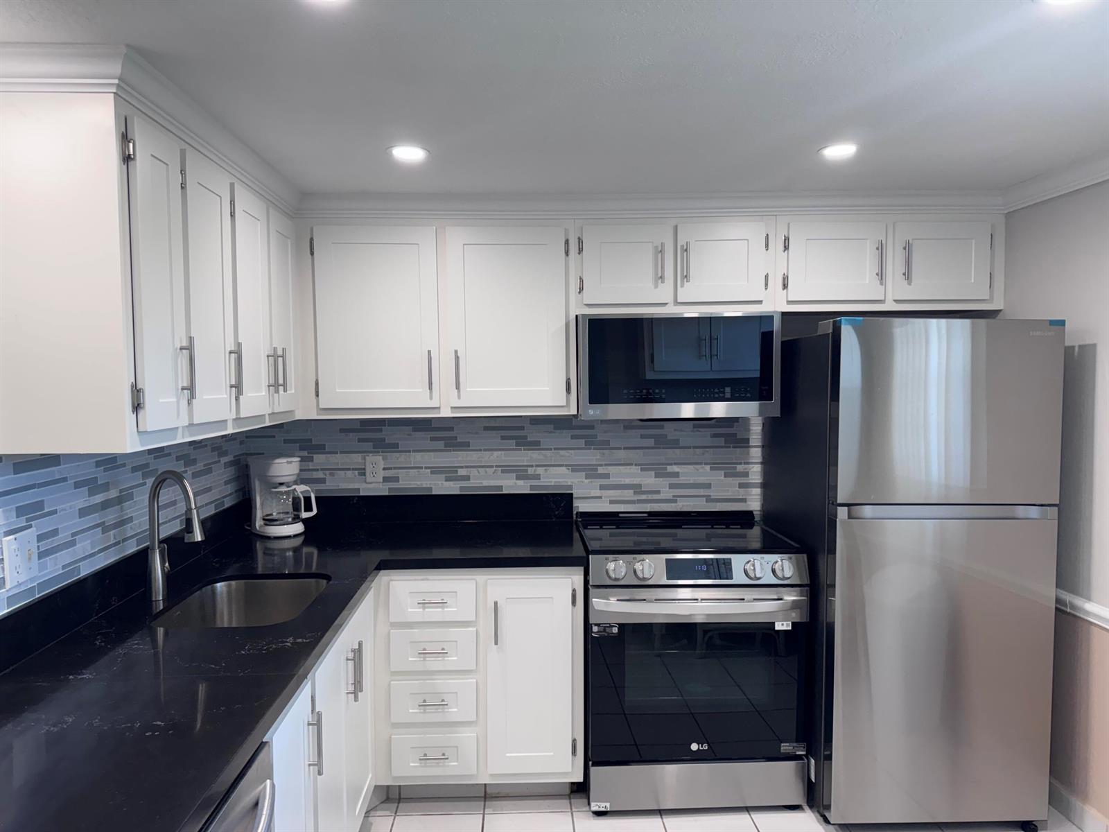 A kitchen features white cabinets, black countertops, a stainless steel refrigerator, and a tiled backsplash — 300 NE 26th Avenue # 4030, Boynton Beach FL 33435, BOYNTON BEACH, FL