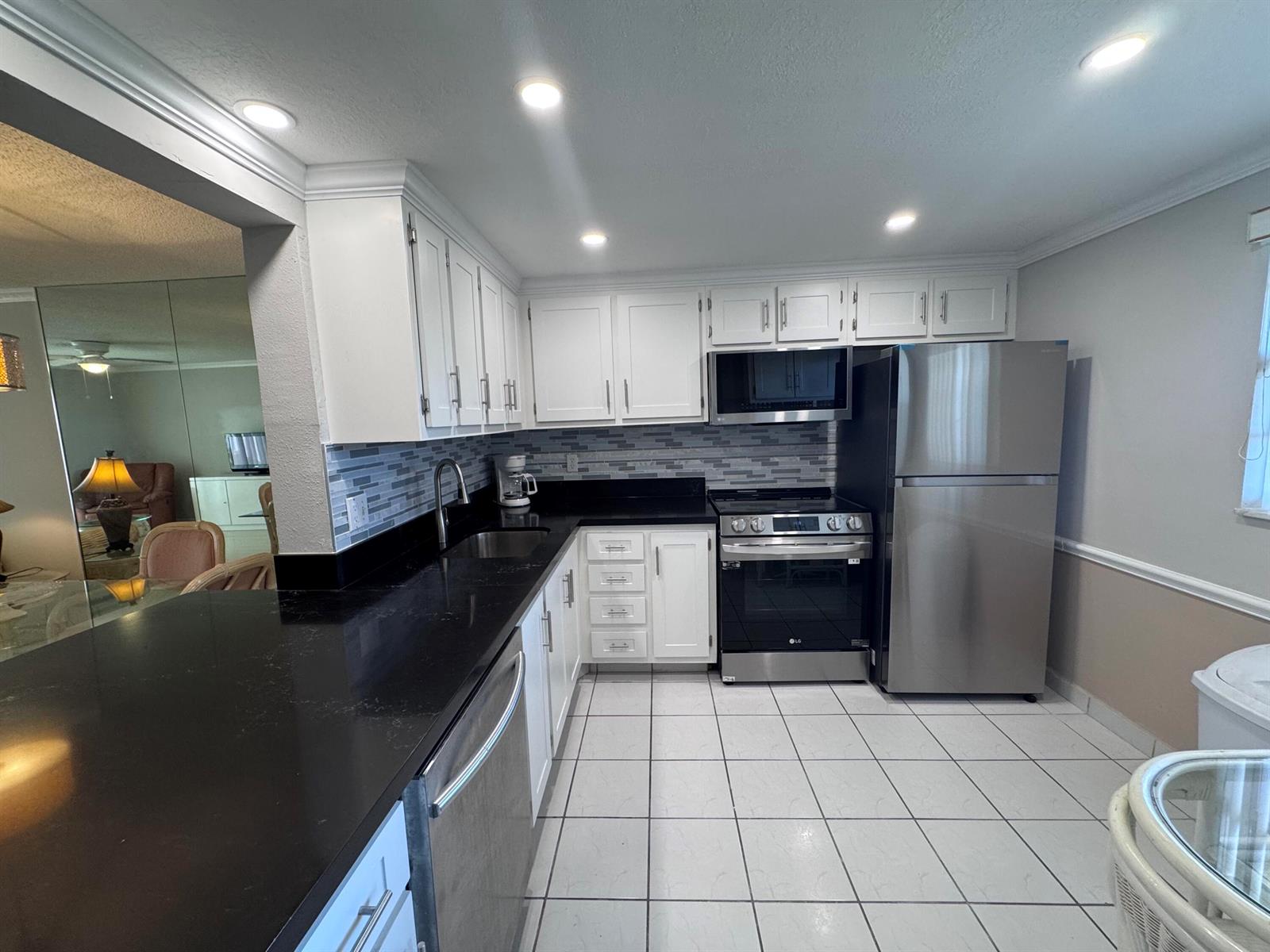 A kitchen features white cabinets, black countertops, stainless steel appliances, and white tile flooring — 300 NE 26th Avenue # 4030, Boynton Beach FL 33435, BOYNTON BEACH, FL