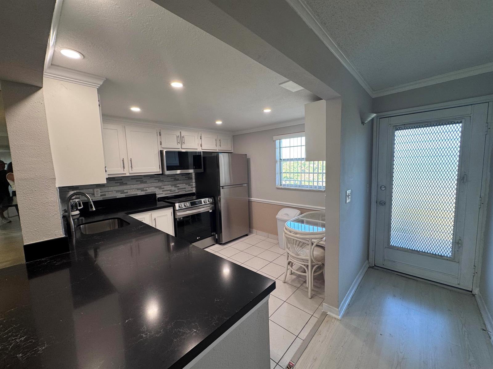 A kitchen features white cabinets, black countertops, stainless steel appliances, and a small dining area — 300 NE 26th Avenue # 4030, Boynton Beach FL 33435, BOYNTON BEACH, FL