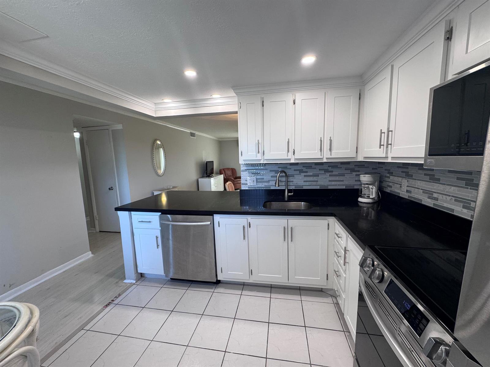 A kitchen features white cabinets, black countertops, stainless steel appliances, and light-colored tile flooring — 300 NE 26th Avenue # 4030, Boynton Beach FL 33435, BOYNTON BEACH, FL