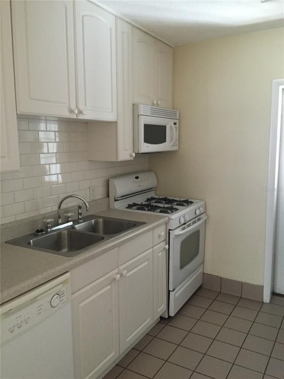 A kitchen features white cabinets, a stainless steel sink, a gas stove, and tiled flooring — 2417 GOLFVIEW STREET, LAKELAND, FL