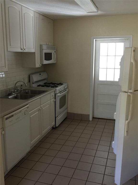 A kitchen features white cabinets, a dishwasher, a gas range, and light-colored tile flooring — 2417 GOLFVIEW STREET, LAKELAND, FL