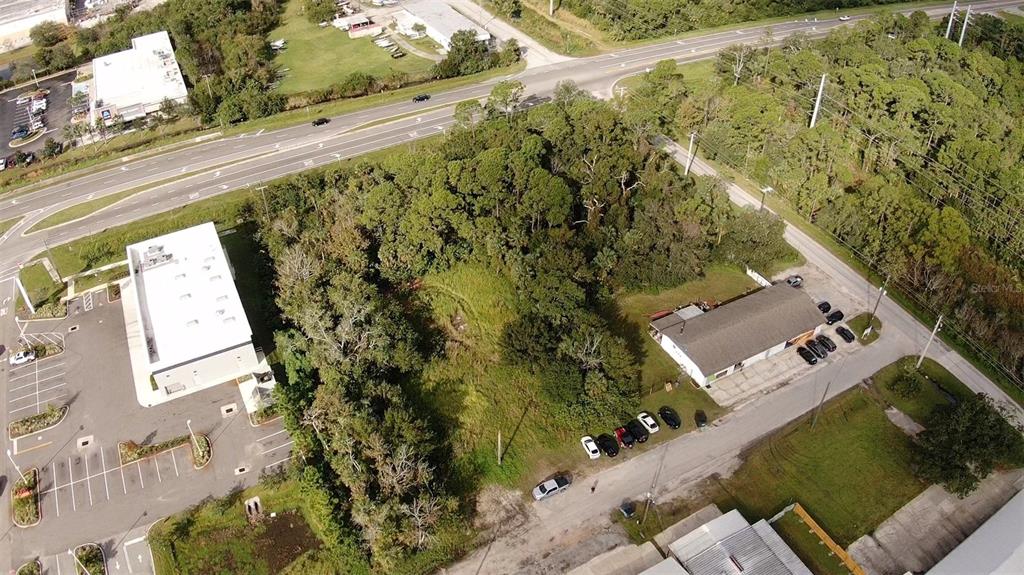 An aerial view shows a wooded lot situated between two commercial buildings and a highway — 4640 CALLE CORTO, TITUSVILLE, FL