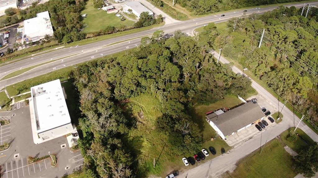 An aerial view shows a wooded lot situated between a commercial building and a parking area — 4640 CALLE CORTO, TITUSVILLE, FL