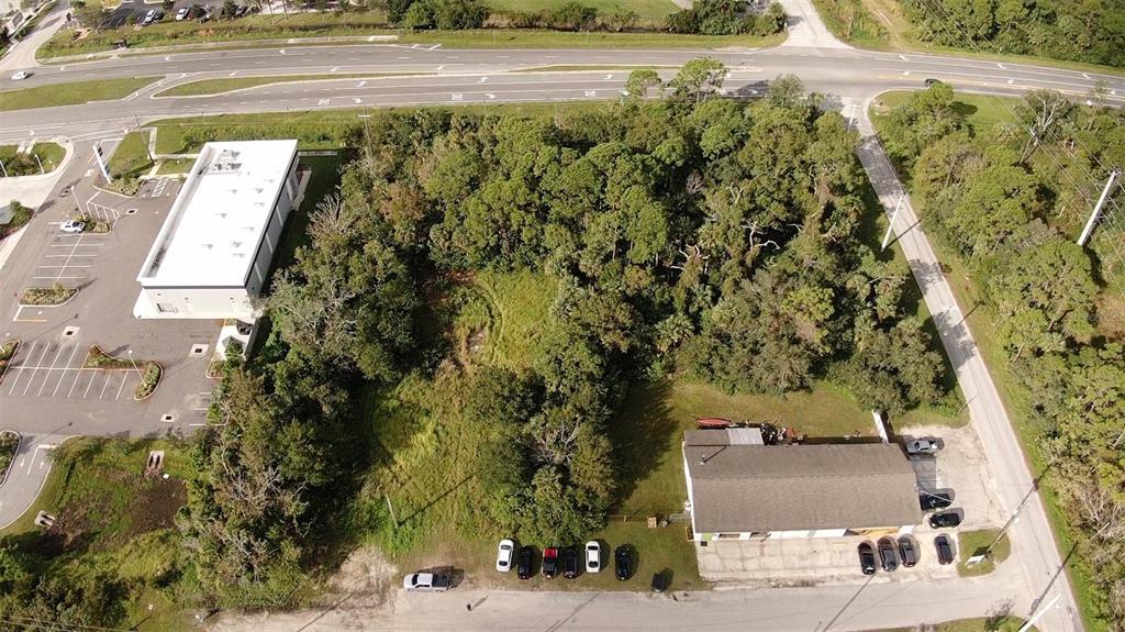 An aerial view shows a wooded lot situated between two commercial buildings and a road — 4640 CALLE CORTO, TITUSVILLE, FL