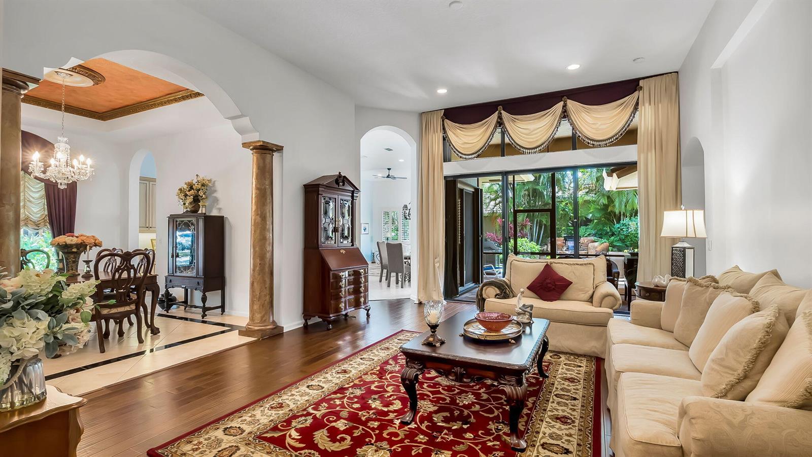 A living room with hardwood floors, a red area rug, and a view of greenery — 11012 Vía Sorrento, Boynton Beach FL 33437, BOYNTON BEACH, FL