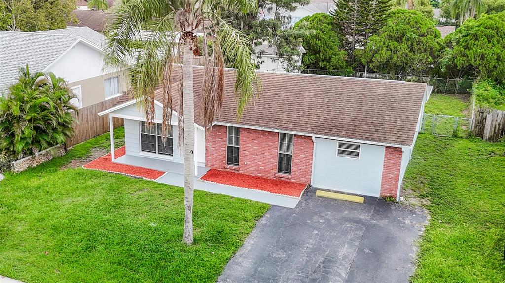 An aerial view of a single-story house with a brick facade, driveway, and palm tree — 7400 MITCHELL RANCH ROAD, NEW PORT RICHEY, FL