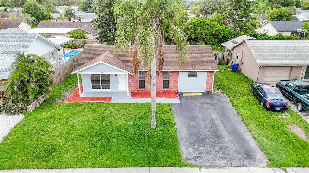 An aerial view shows a single-story house with a brick facade, palm tree, and driveway — 7400 MITCHELL RANCH ROAD, NEW PORT RICHEY, FL