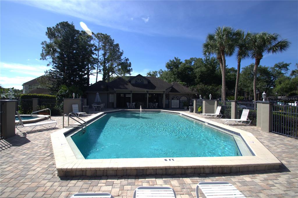 An outdoor swimming pool with a paved deck and a clubhouse in the background — 939 FRAMLINGHAM COURT UNIT 103, LAKE MARY, FL