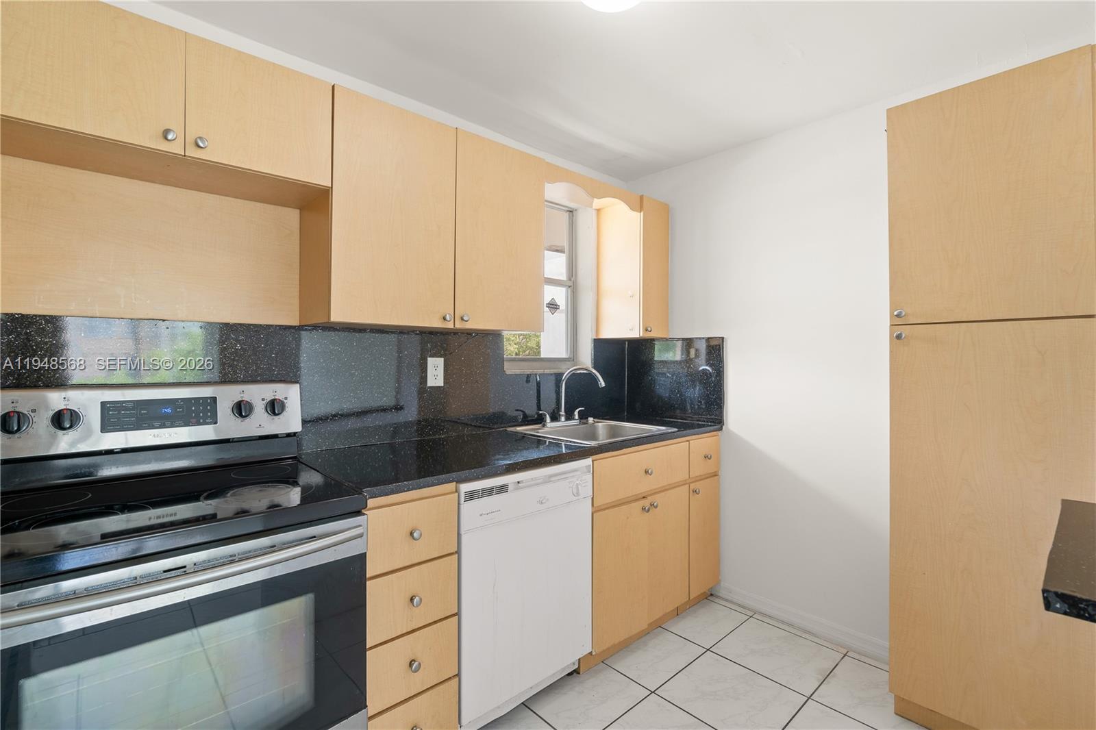 A kitchen features light wood cabinets, black countertops, a stove, and a white dishwasher — 1700 NE 191st St # 202, Miami FL 33179, MIAMI, FL