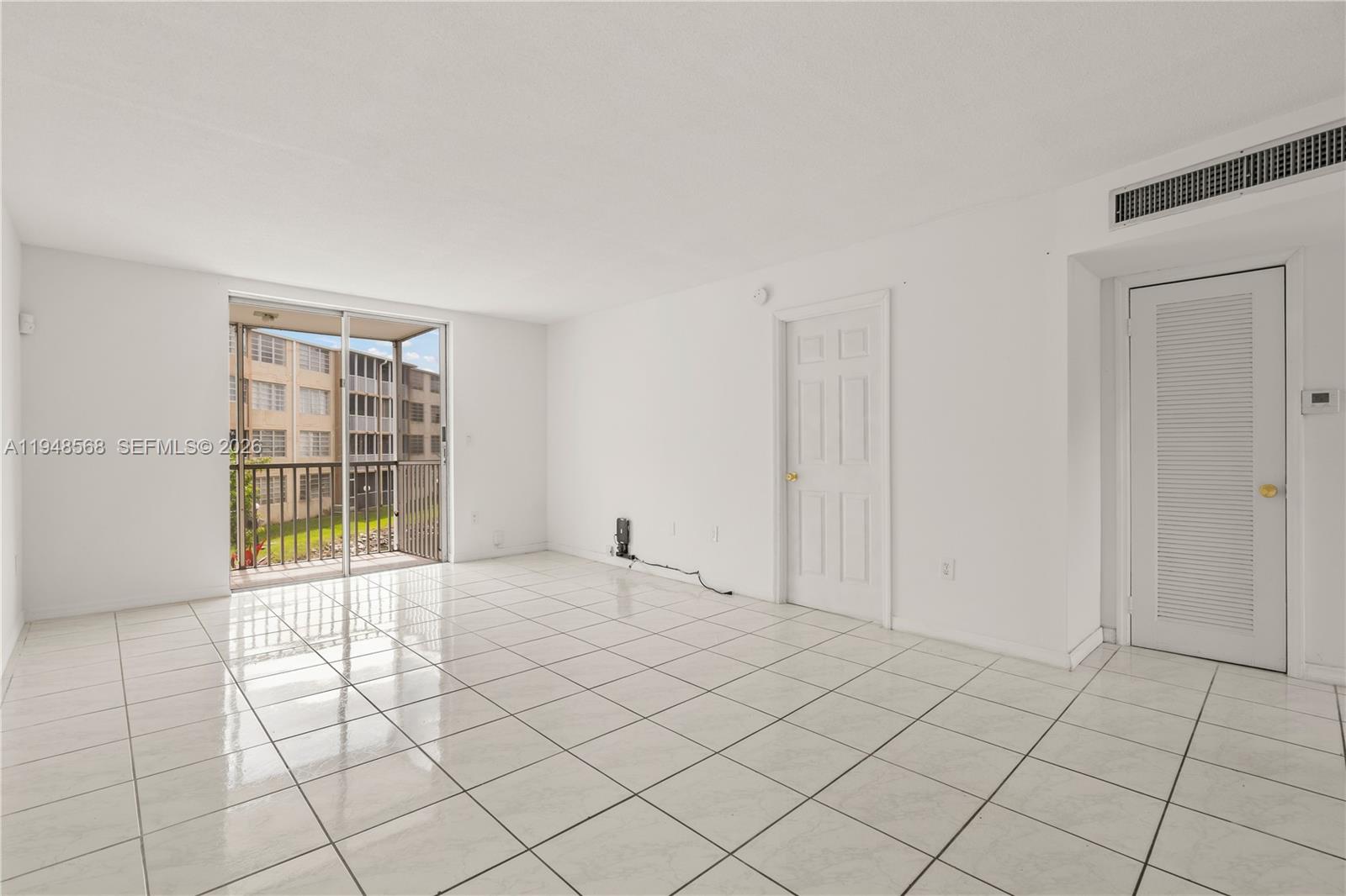 An empty room with white tile flooring, a sliding glass door, and two white doors — 1700 NE 191st St # 202, Miami FL 33179, MIAMI, FL