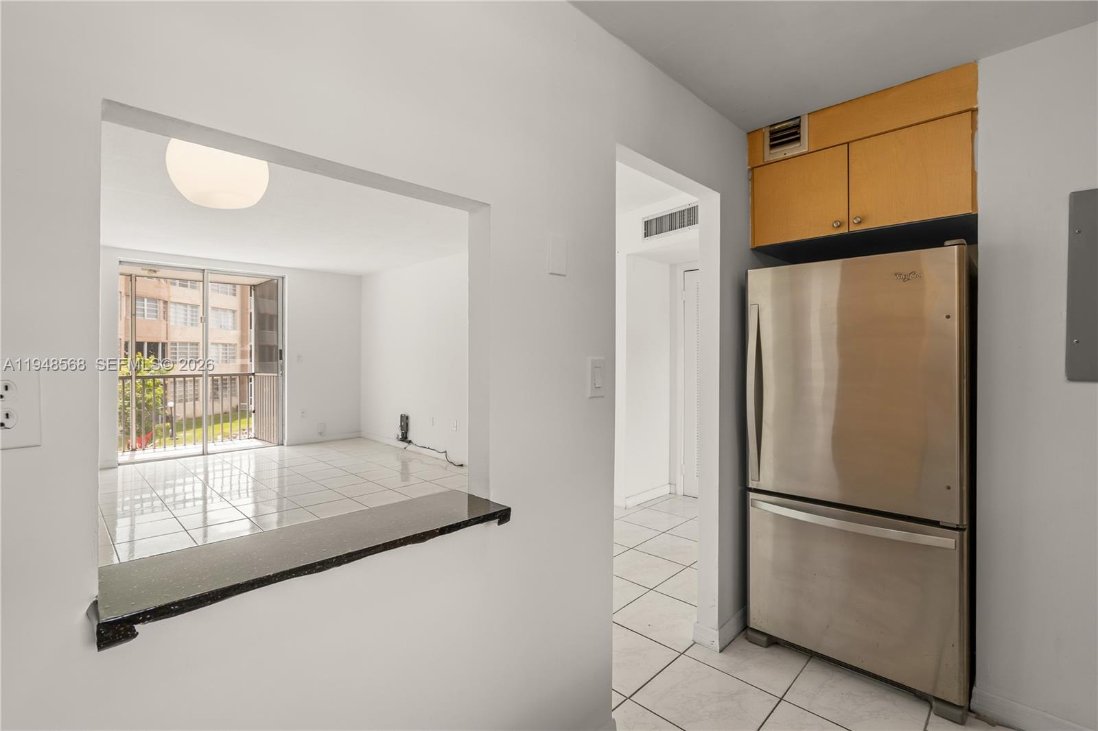 A kitchen features a stainless steel refrigerator, light wood cabinets, and a pass-through window — 1700 NE 191st St # 202, Miami FL 33179, MIAMI, FL
