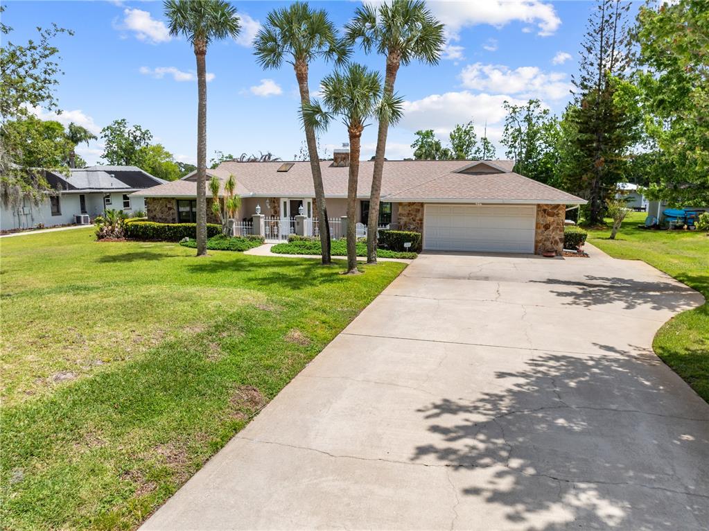 A single-story house with a stone facade, a two-car garage, and palm trees in front — 6770 BAY SHORE DRIVE, ST CLOUD, FL