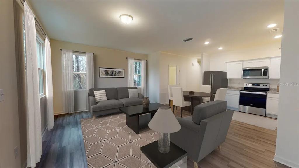 An open-concept living and dining area features wood-look flooring, a gray sofa, and kitchen appliances — 14876 LUCCA WAY, DADE CITY, FL