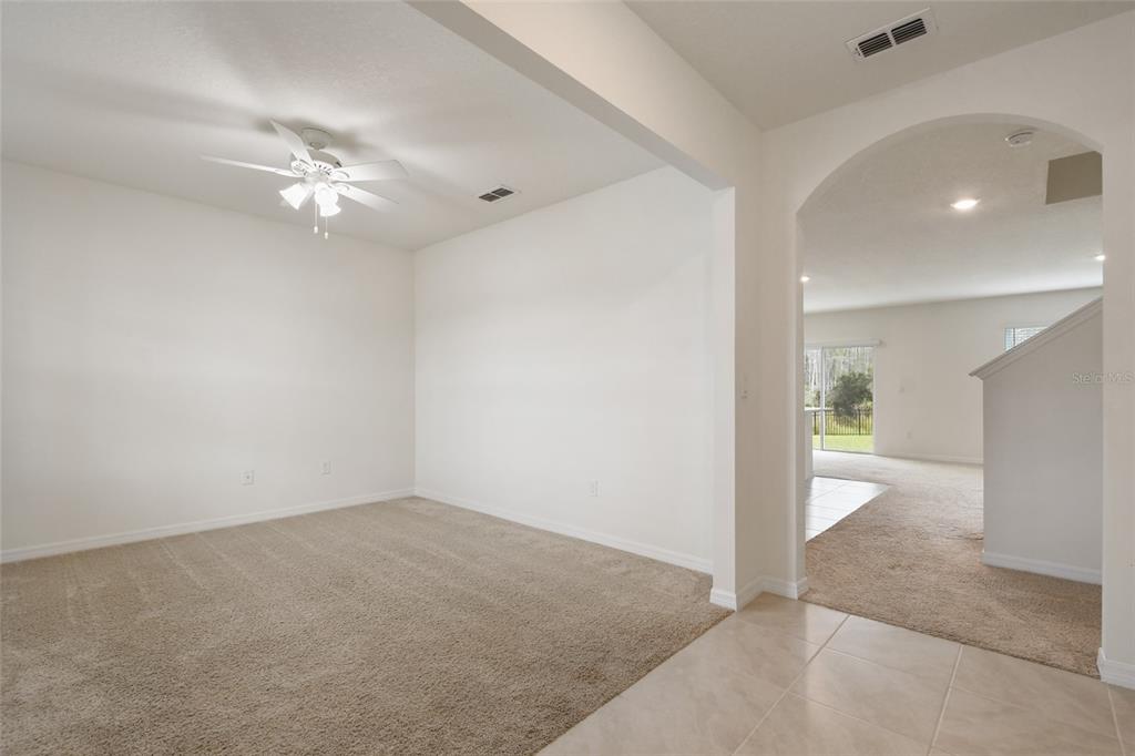 A carpeted room with a ceiling fan connects to an adjacent living area through an archway — 1363 FOX SQUIRREL DRIVE, DAVENPORT, FL