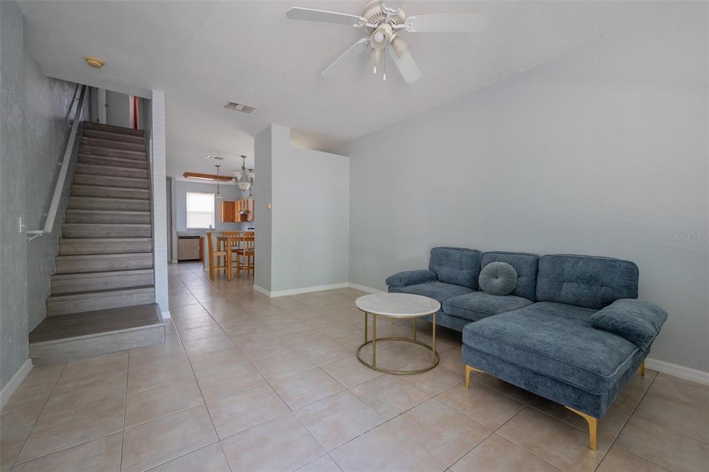 A living room with tile flooring, a blue sectional sofa, and stairs leading to another level — 3860 SW 20TH AVENUE UNIT 1808, GAINESVILLE, FL