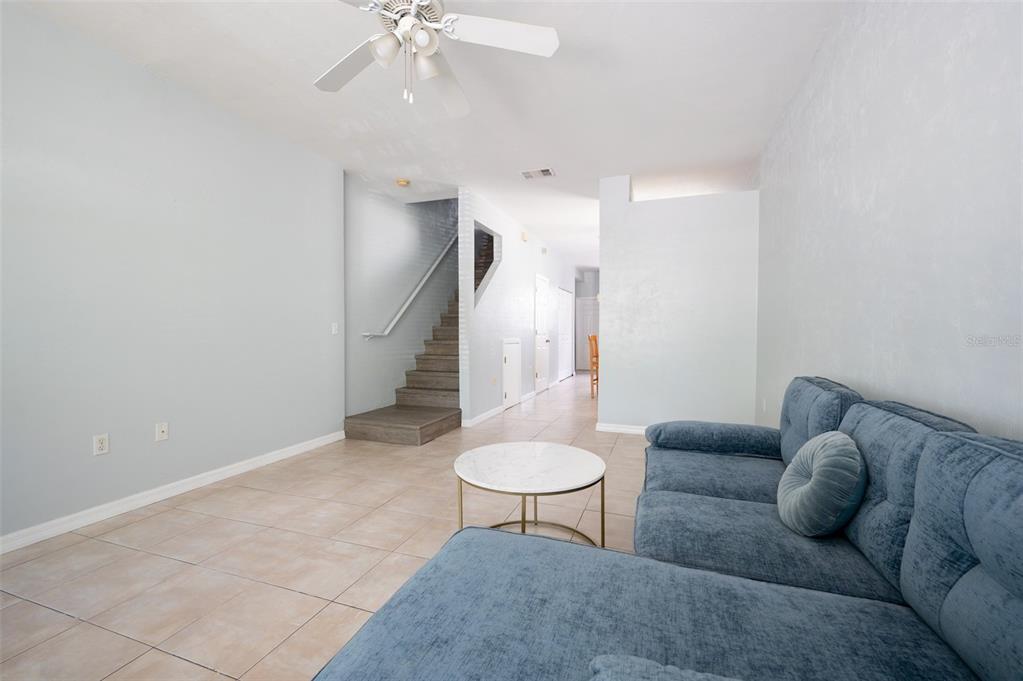 A living room features light tile flooring, a blue sectional sofa, and a wooden staircase — 3860 SW 20TH AVENUE UNIT 1808, GAINESVILLE, FL