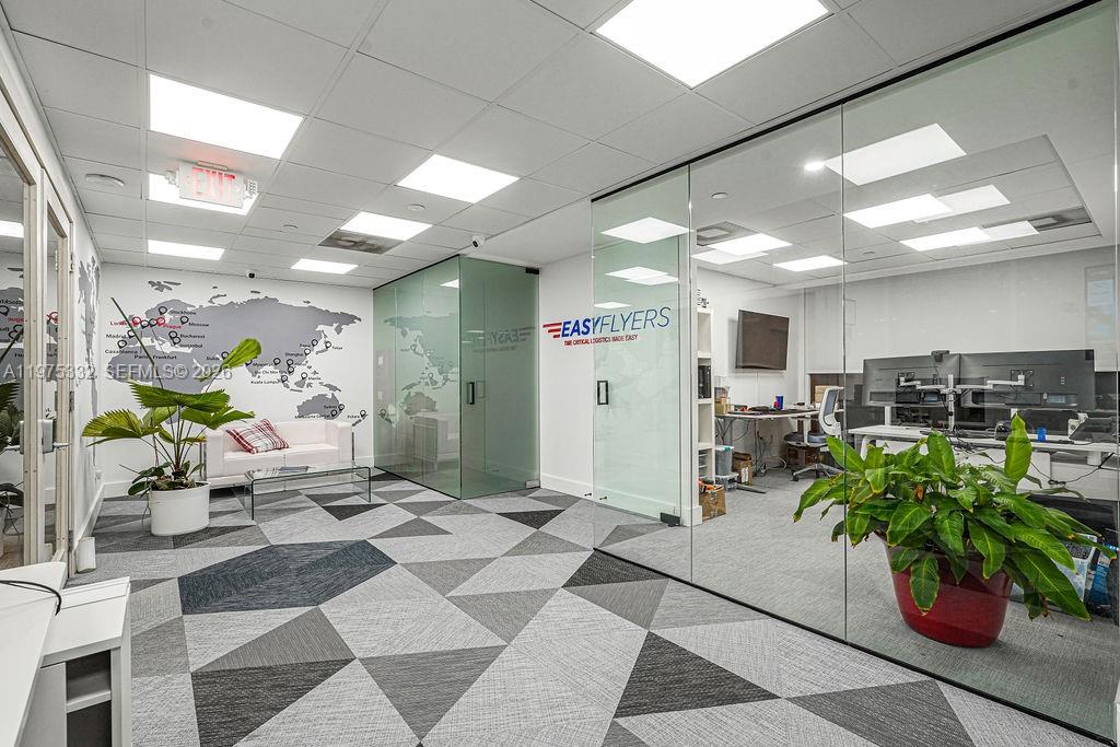 A modern office space features a world map wall, glass-enclosed rooms, and geometric patterned flooring — 1110 Brickell Ave # 700A, Miami FL 33131, MIAMI, FL