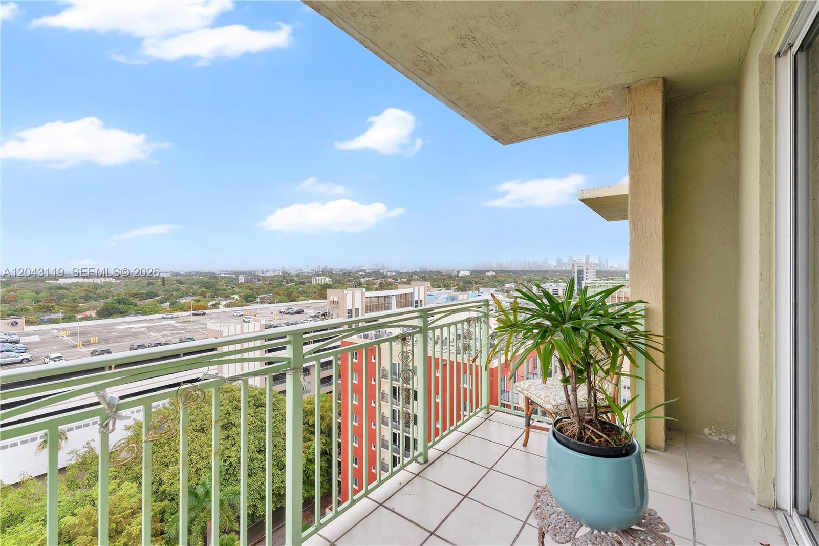 A balcony with a tiled floor, green metal railing, and a potted plant overlooks buildings — 3500 Coral Way # 10, Miami FL 33145, MIAMI, FL