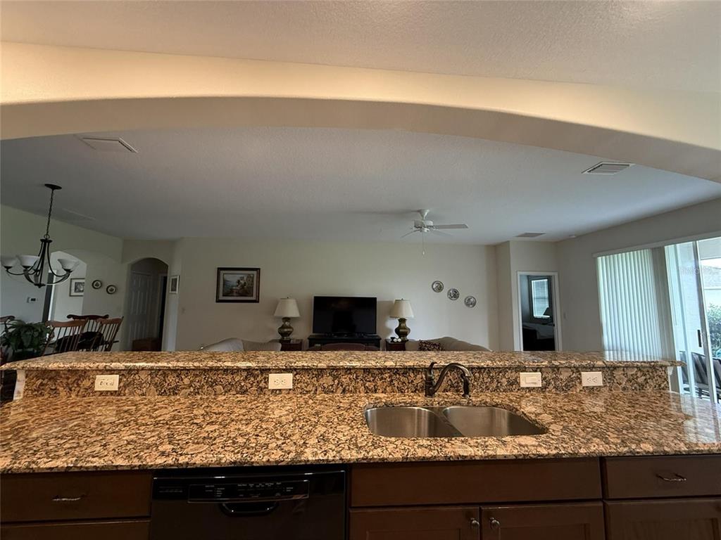 A kitchen with granite countertops and a double sink overlooks a living room area — 4546 SHENANDOAH RIVER TRAIL, LEESBURG, FL