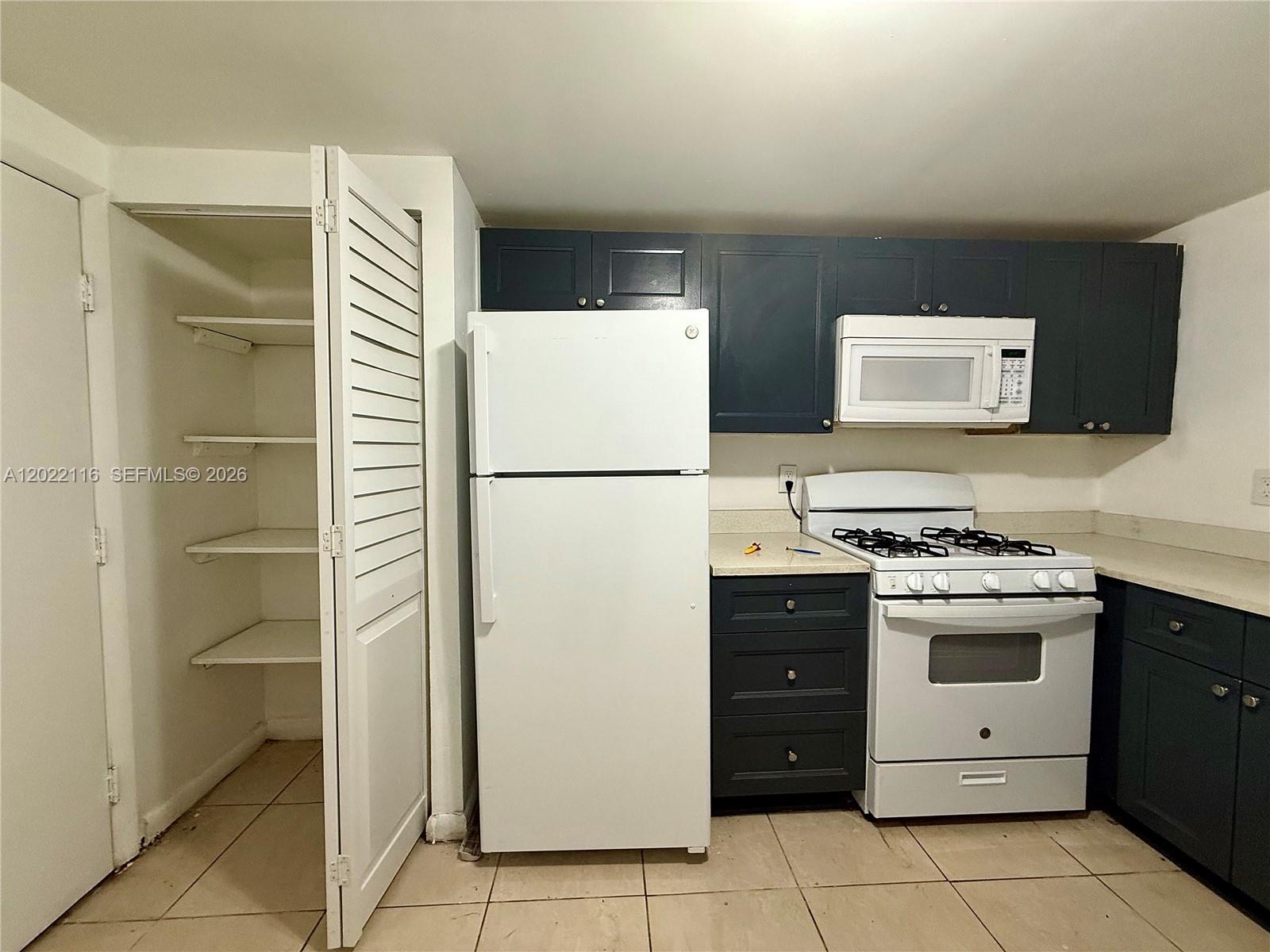 A kitchen features dark blue cabinets, white appliances, and a pantry with open shelving — 18101 NW 68th Ave # B102, Hialeah FL 33015, HIALEAH, FL