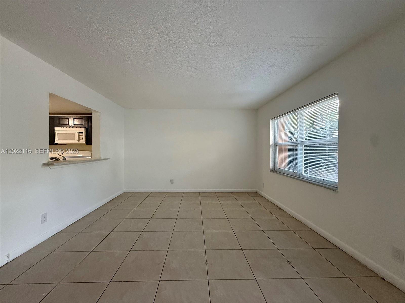 An empty room features beige tile flooring, white walls, and a window with blinds — 18101 NW 68th Ave # B102, Hialeah FL 33015, HIALEAH, FL