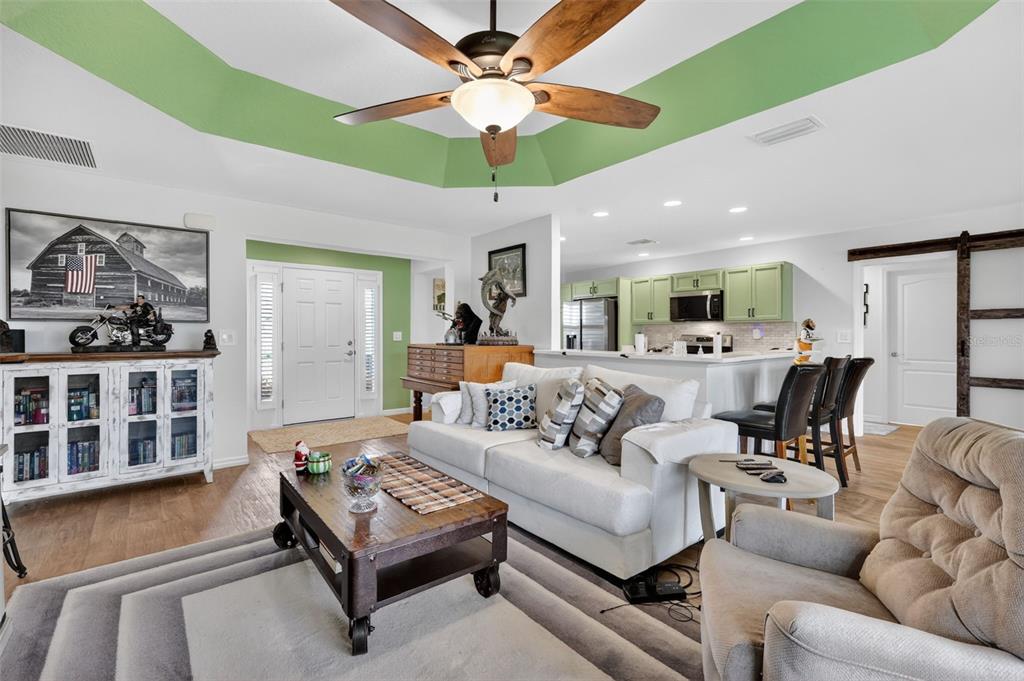 A living room with a tray ceiling, white sofa, coffee table, and an open kitchen — 11367 LAUFERSKY LANE, OXFORD, FL