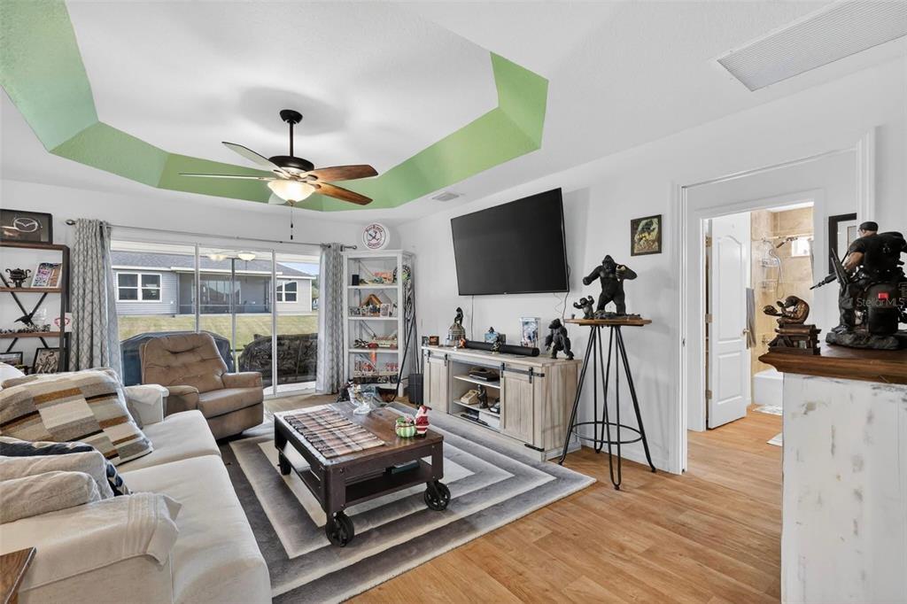 A living room features a green tray ceiling, wood-look flooring, and a sliding glass door — 11367 LAUFERSKY LANE, OXFORD, FL