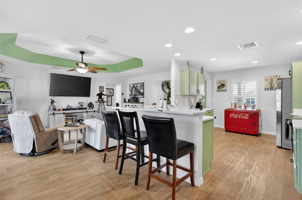 An open-concept living room and kitchen area with light wood flooring and green accents — 11367 LAUFERSKY LANE, OXFORD, FL