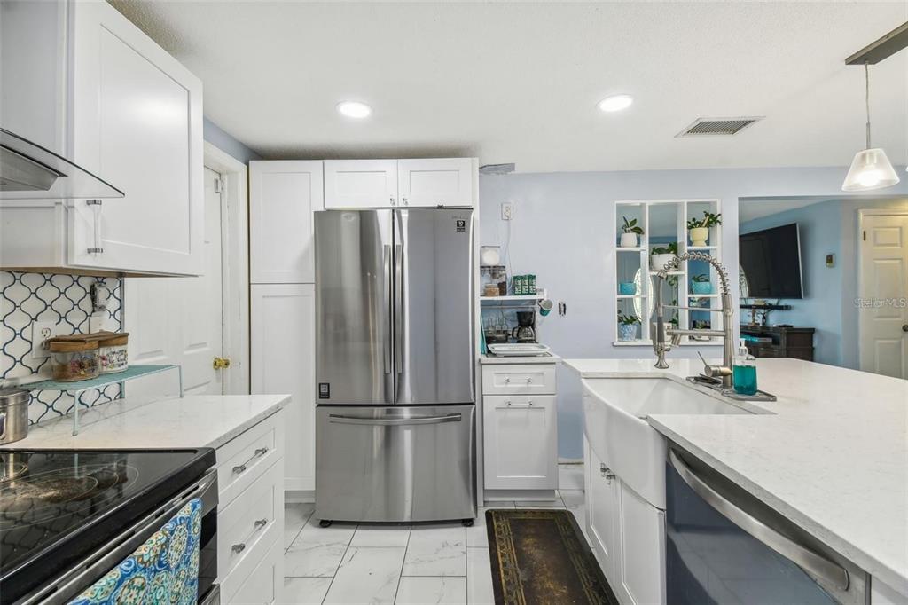A bright kitchen features white cabinets, a central island, stainless steel appliances, and marble-look tile — 1627 DANDER DRIVE, HOLIDAY, FL
