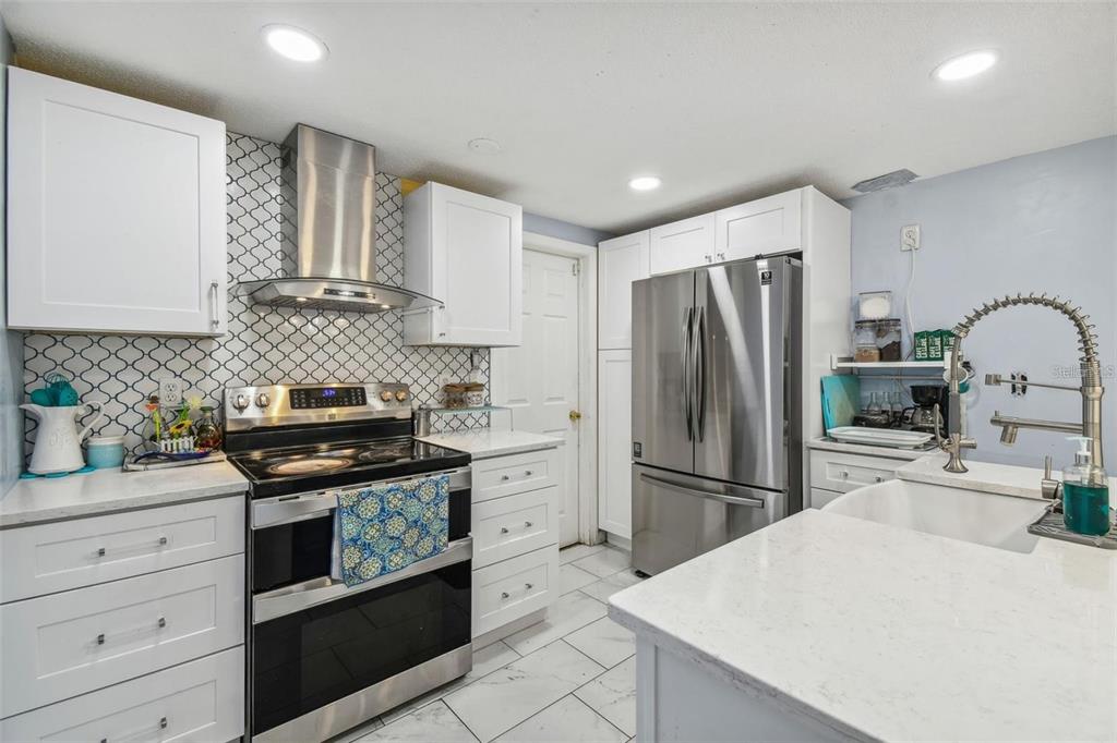 A modern kitchen features white cabinetry, stainless steel appliances, a central island, and tiled flooring — 1627 DANDER DRIVE, HOLIDAY, FL