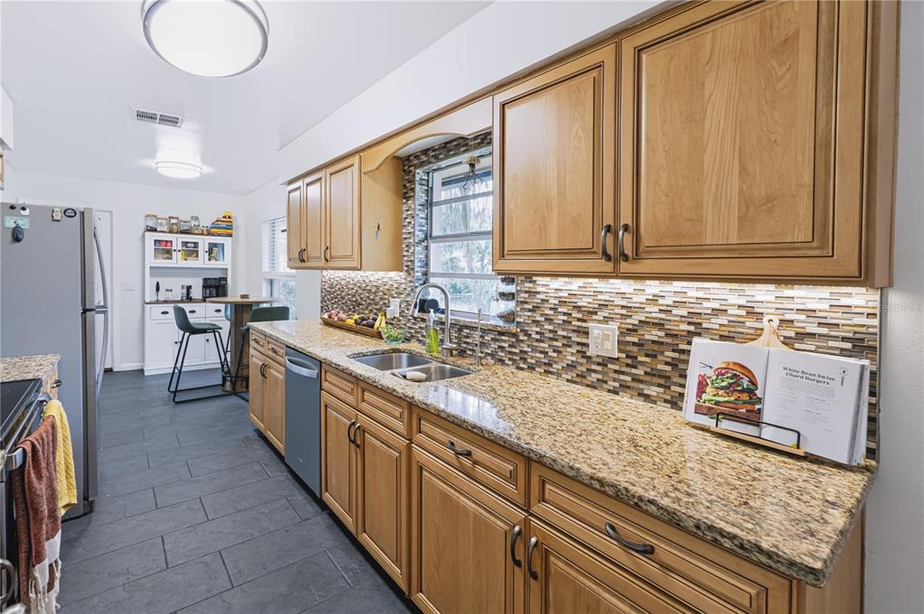 A kitchen features oak cabinets, granite countertops, a mosaic tile backsplash, and dark tile flooring — 241 RUTH BOULEVARD, LONGWOOD, FL