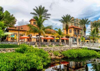 A waterfront restaurant building with palm trees, outdoor patio seating, and colorful umbrellas — 102 RIVIERA DUNES WAY UNIT S-88, PALMETTO, FL