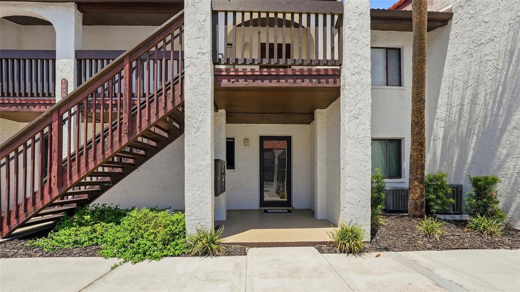 An exterior view of a two-story apartment building with a wooden staircase and front entrance — 1638 STICKNEY POINT ROAD UNIT 38-102, SARASOTA, FL