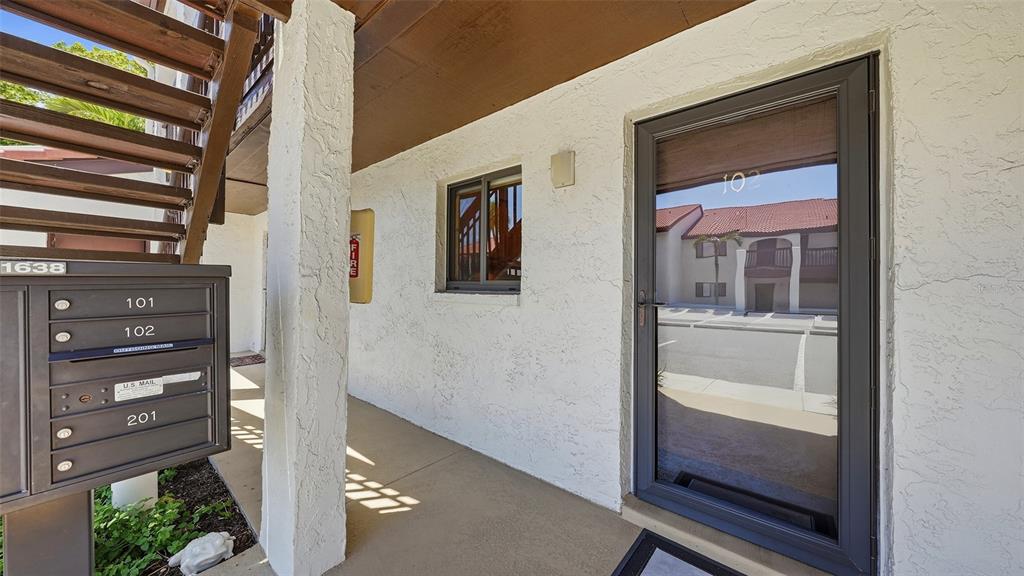 An exterior view of a building entrance featuring a glass door, mailboxes, and a staircase — 1638 STICKNEY POINT ROAD UNIT 38-102, SARASOTA, FL