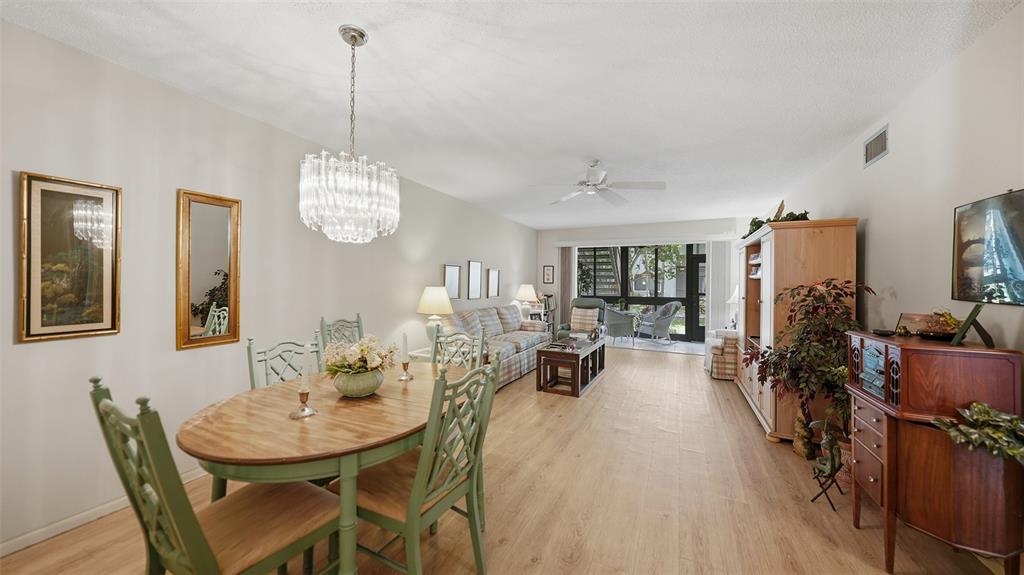 A dining area and living room with light wood flooring, a chandelier, and patio access — 1638 STICKNEY POINT ROAD UNIT 38-102, SARASOTA, FL
