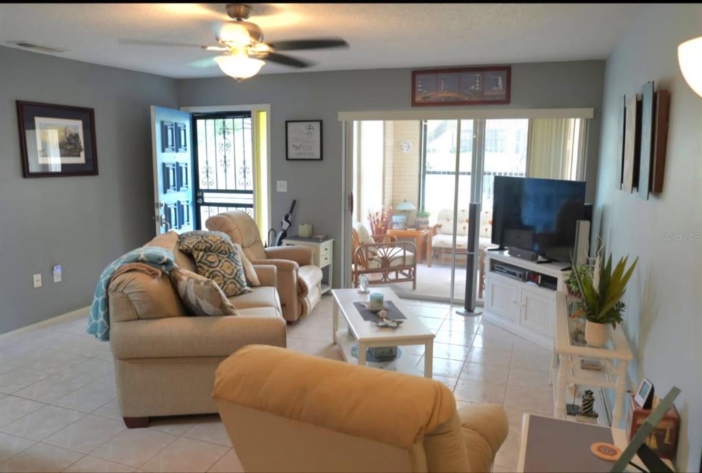 A living room with tile floors, a ceiling fan, a sofa, and a sliding glass door — 8141 BUGLE COURT UNIT 2, PORT RICHEY, FL
