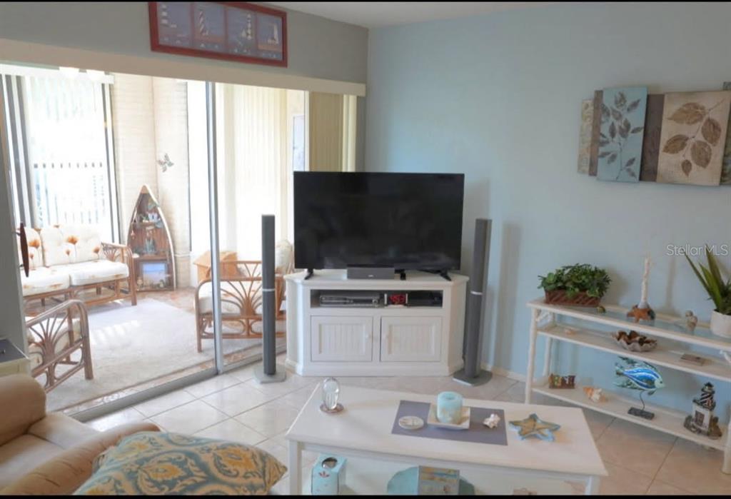 A living room with a television on a white stand, tile floors, and a sunroom — 8141 BUGLE COURT UNIT 2, PORT RICHEY, FL