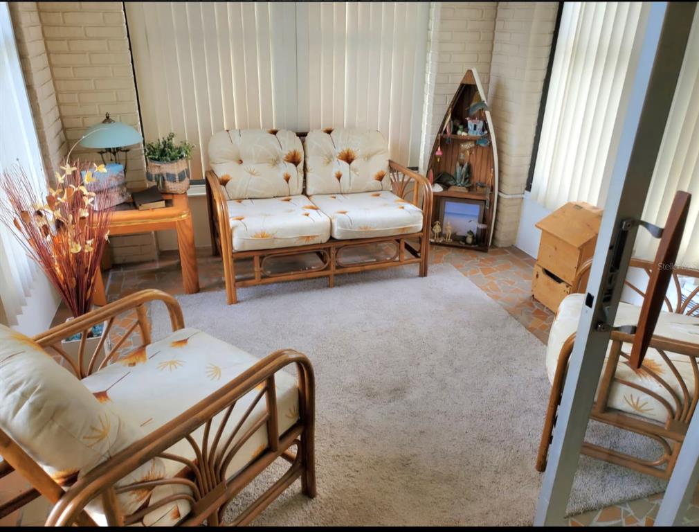 A sunroom features rattan furniture with floral cushions, a boat-shaped shelf, and brick walls — 8141 BUGLE COURT UNIT 2, PORT RICHEY, FL