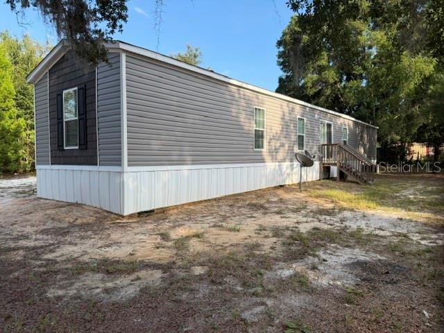 A gray manufactured home with white skirting and a wooden deck sits on a dirt lot — 113 MAGNOLIA AVENUE, HAWTHORNE, FL