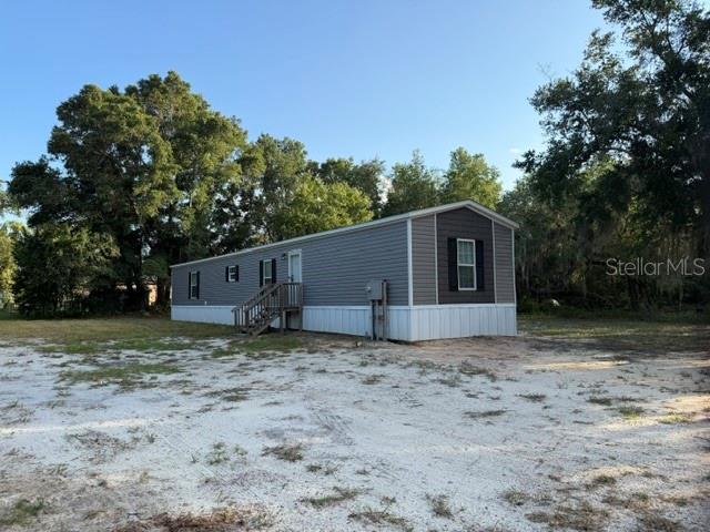 A gray manufactured home sits on a sandy lot surrounded by trees — 113 MAGNOLIA AVENUE, HAWTHORNE, FL