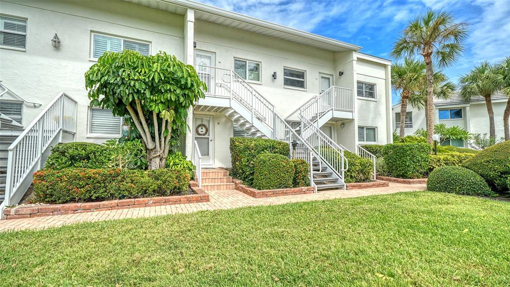 A two-story apartment building features white stucco walls, exterior staircases, and landscaped shrubbery — 7115 GULF OF MEXICO DRIVE UNIT 23, LONGBOAT KEY, FL