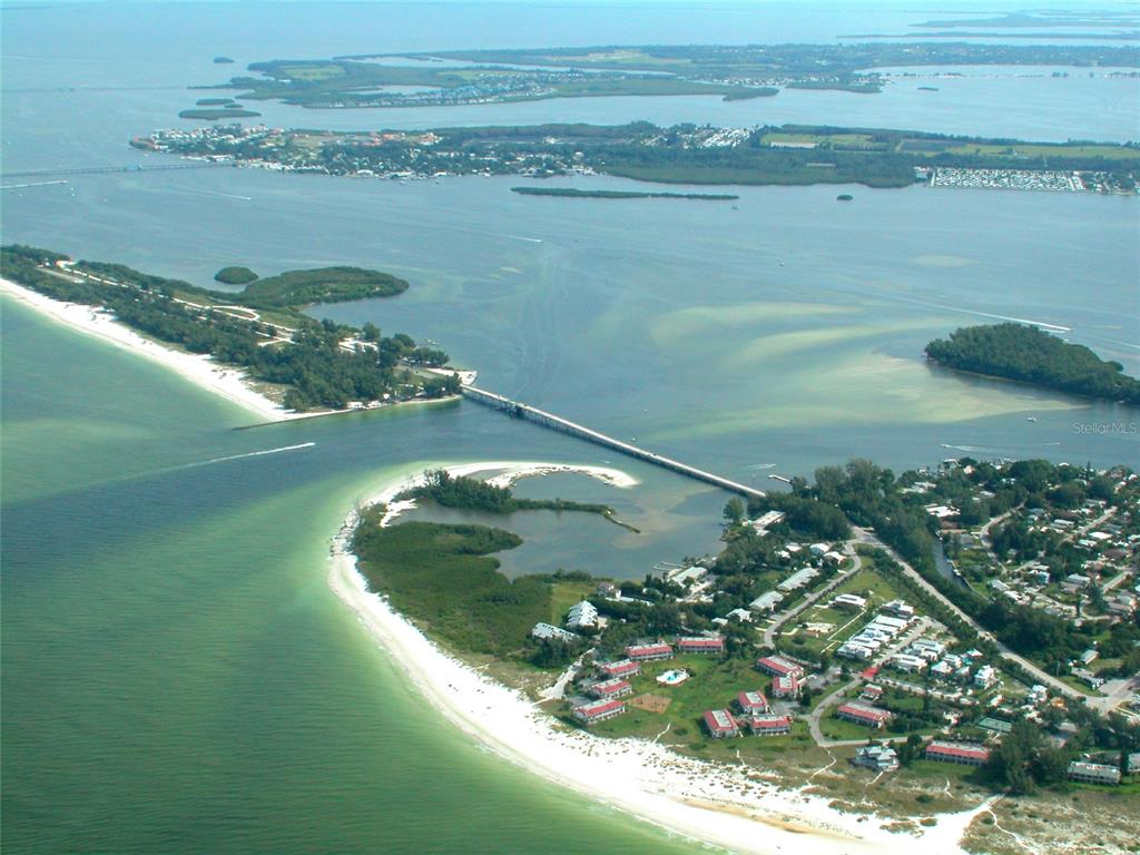An aerial view shows a bridge connecting a sandy beach to a coastal residential area — 7115 GULF OF MEXICO DRIVE UNIT 23, LONGBOAT KEY, FL