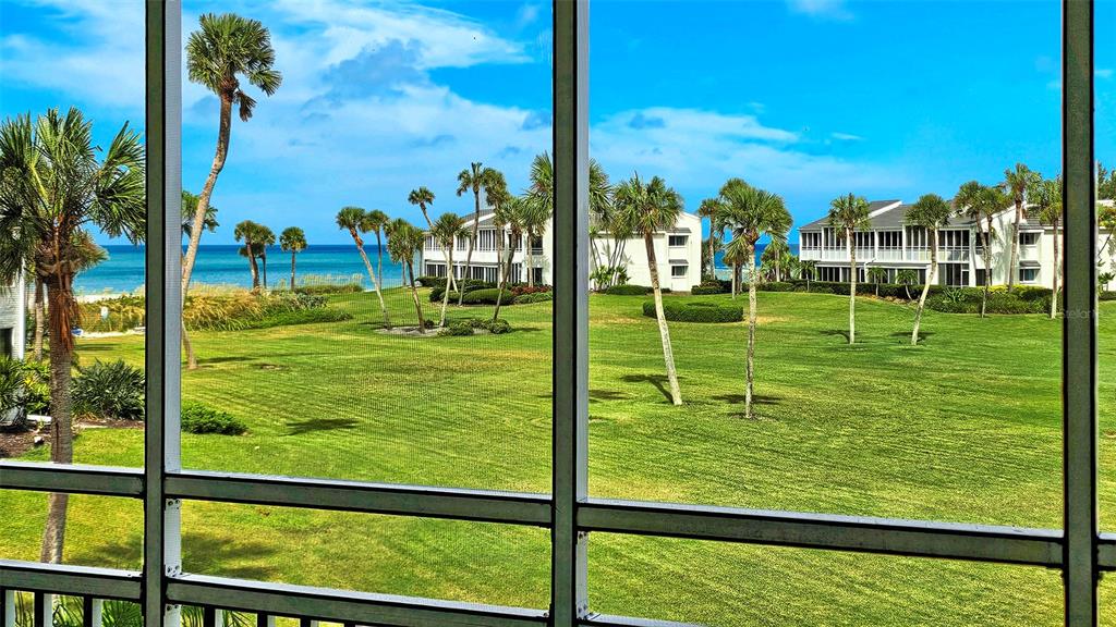 A view of a grassy lawn and ocean from a screened-in balcony — 7115 GULF OF MEXICO DRIVE UNIT 23, LONGBOAT KEY, FL